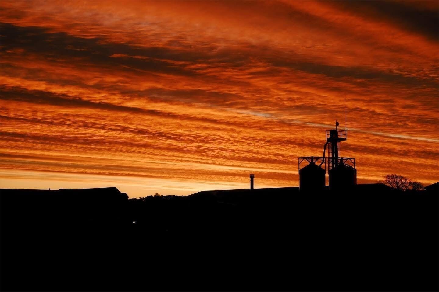 A silhouette of a building with a prominent tower and two cylindrical structures against a sunset sky.