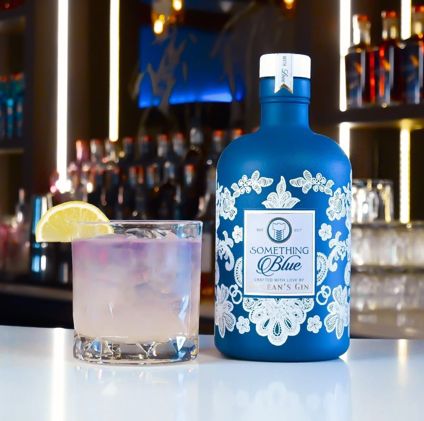 A blue bottle with a label and a glass with a lemon slice on a bar counter.