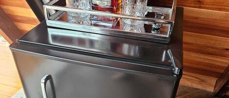 Ein kompakter, schwarzer Kühlschrank mit integrierter Bar, inklusive Flasche und Gläsern.