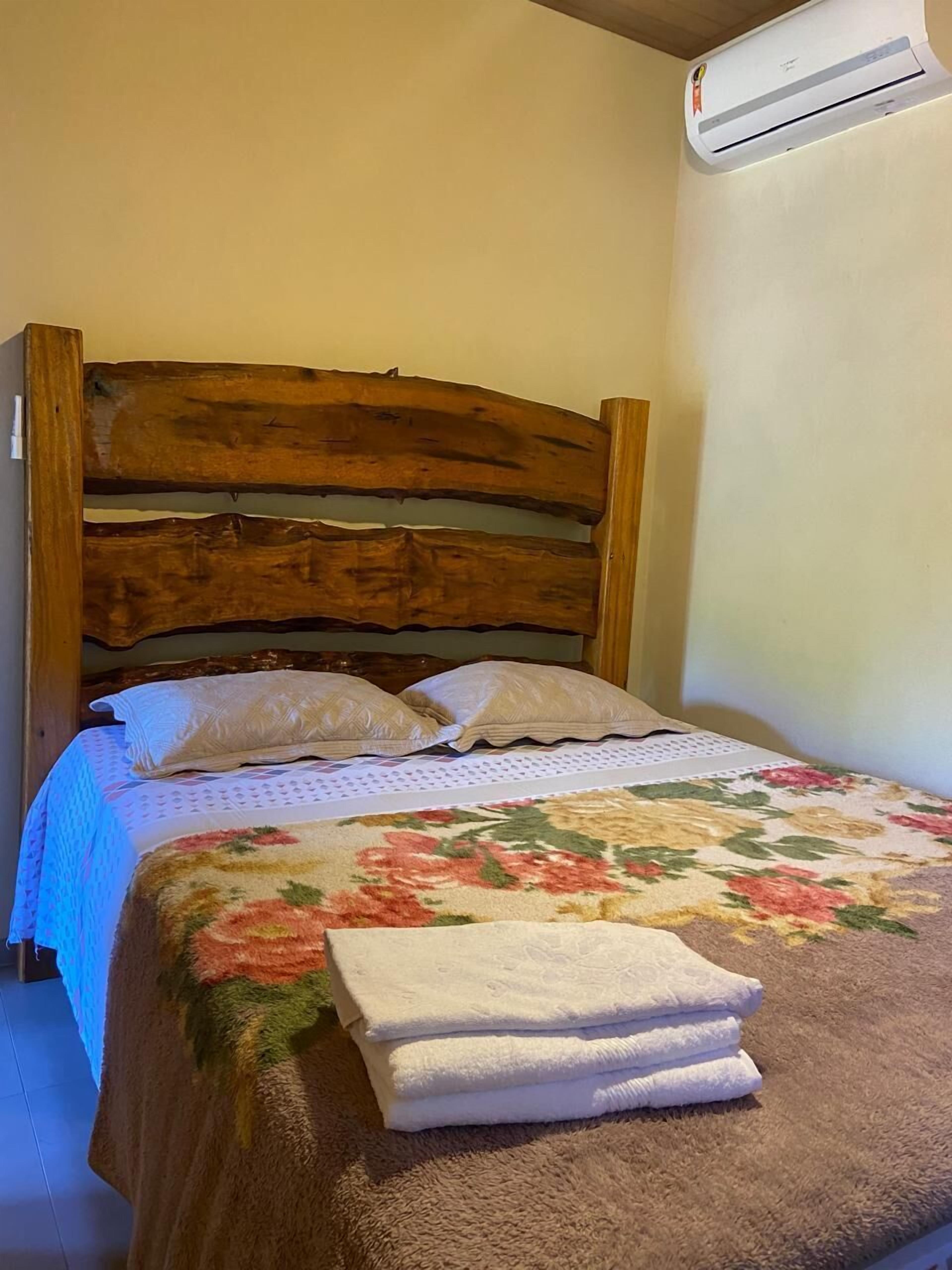 A bed with a wooden headboard, white pillows, a floral bedspread, and a stack of white towels.