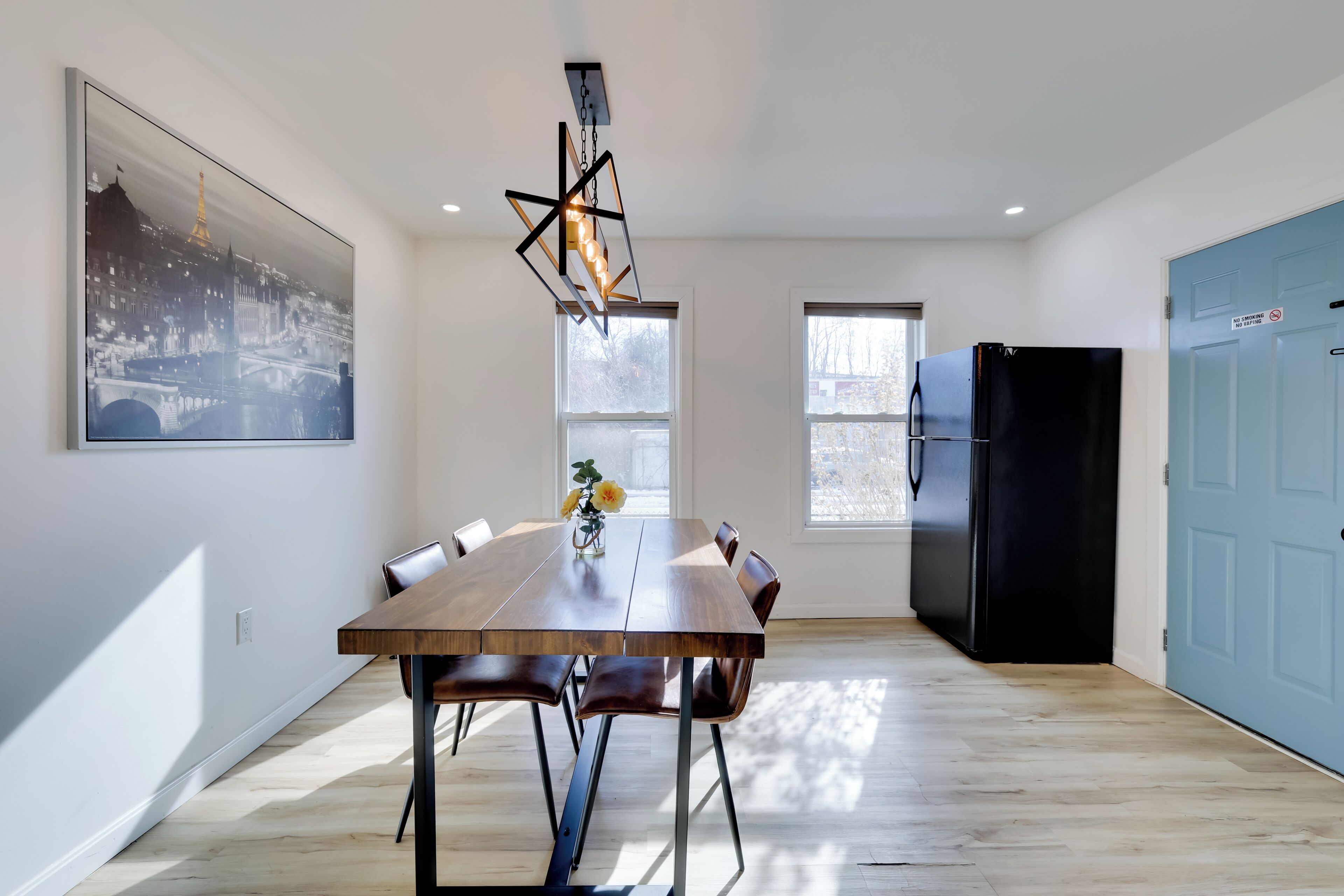 Una cocina moderna con una mesa de comedor, sillas, un refrigerador negro y un ventanal grande.