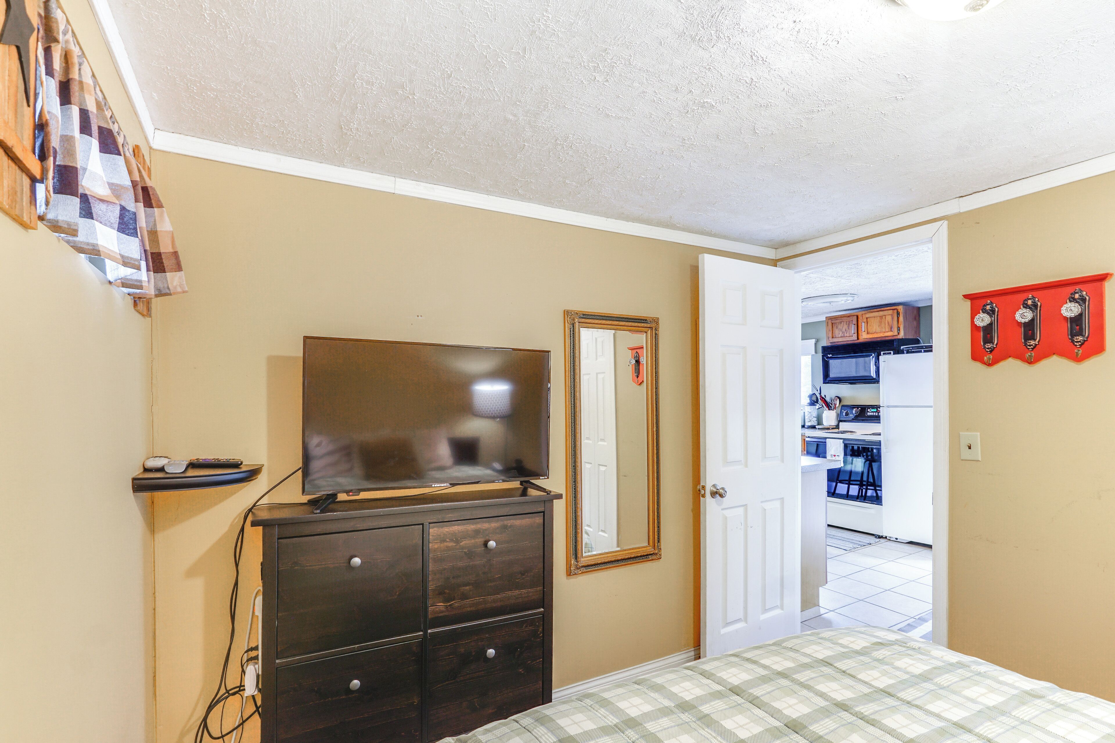 Un dormitorio con cama, cómoda, televisor y puerta que da a una cocina.