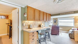 A kitchen with wooden cabinets, a countertop, and bar stools. There is a window with a view of the outside. - Private Boat Dock: Lakefront Cabin in Camdenton (Camdenton)
