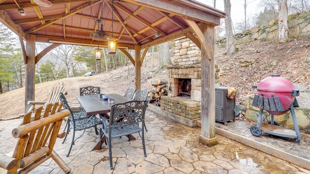 A covered outdoor patio with a stone table and metal chairs, a stone fireplace, and a portable grill. - Private Boat Dock: Lakefront Cabin in Camdenton (Camdenton)