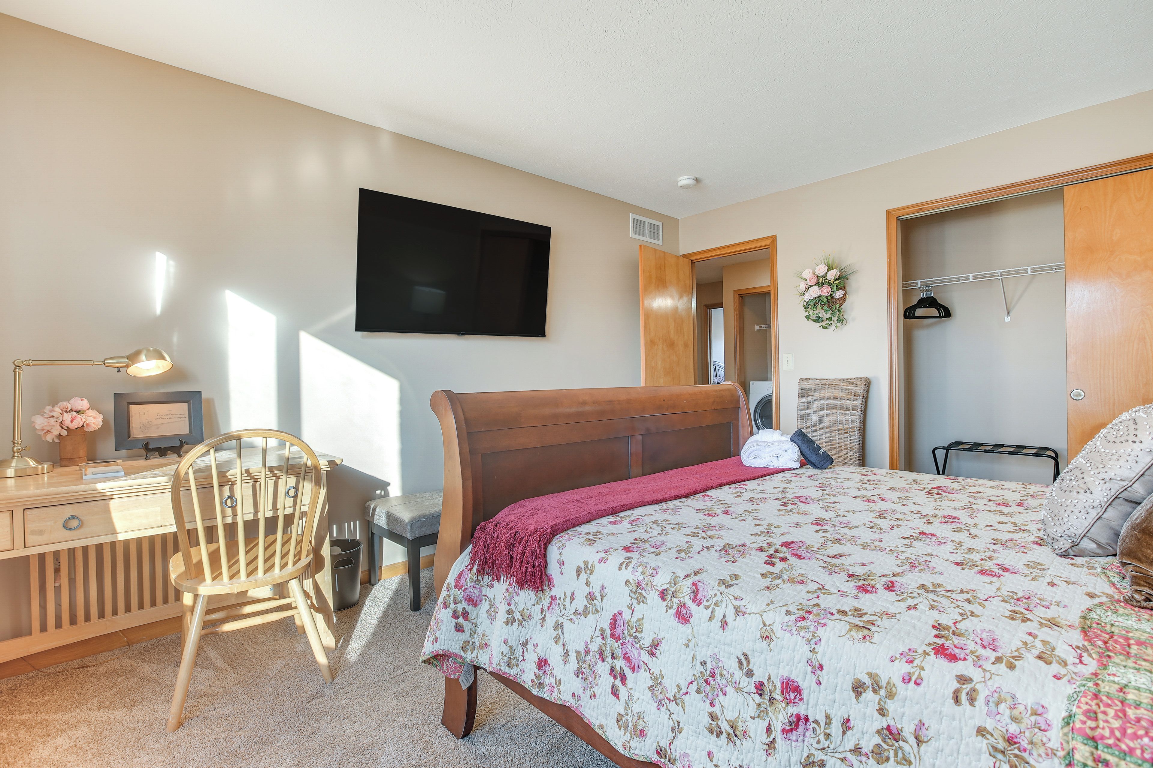 A bedroom with a wooden bed, a desk with a chair, a TV mounted on the wall, and a closet with a hanging rod.