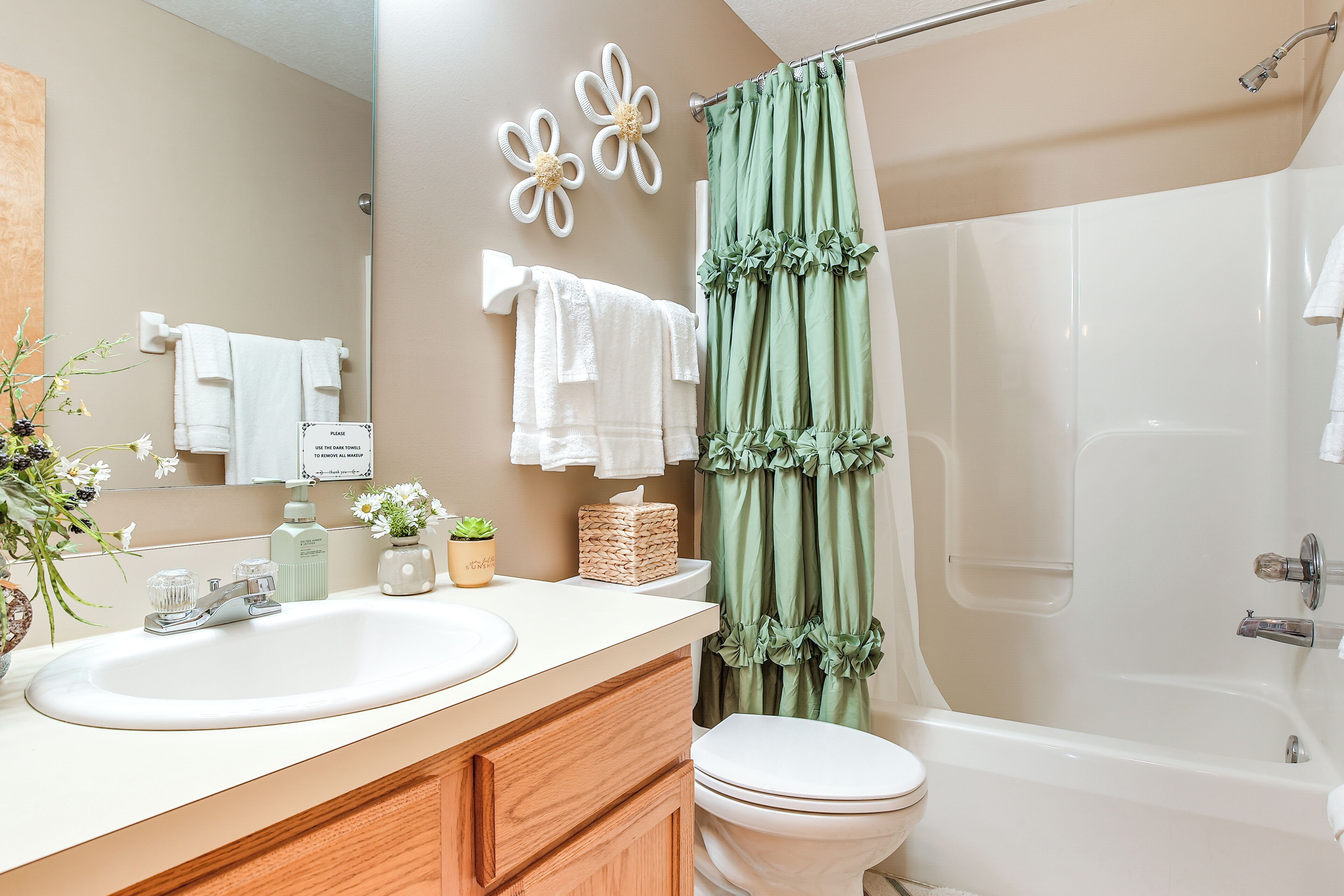 A bathroom with a white sink, a toilet, a shower with a green curtain, and decorative flowers on the wall.