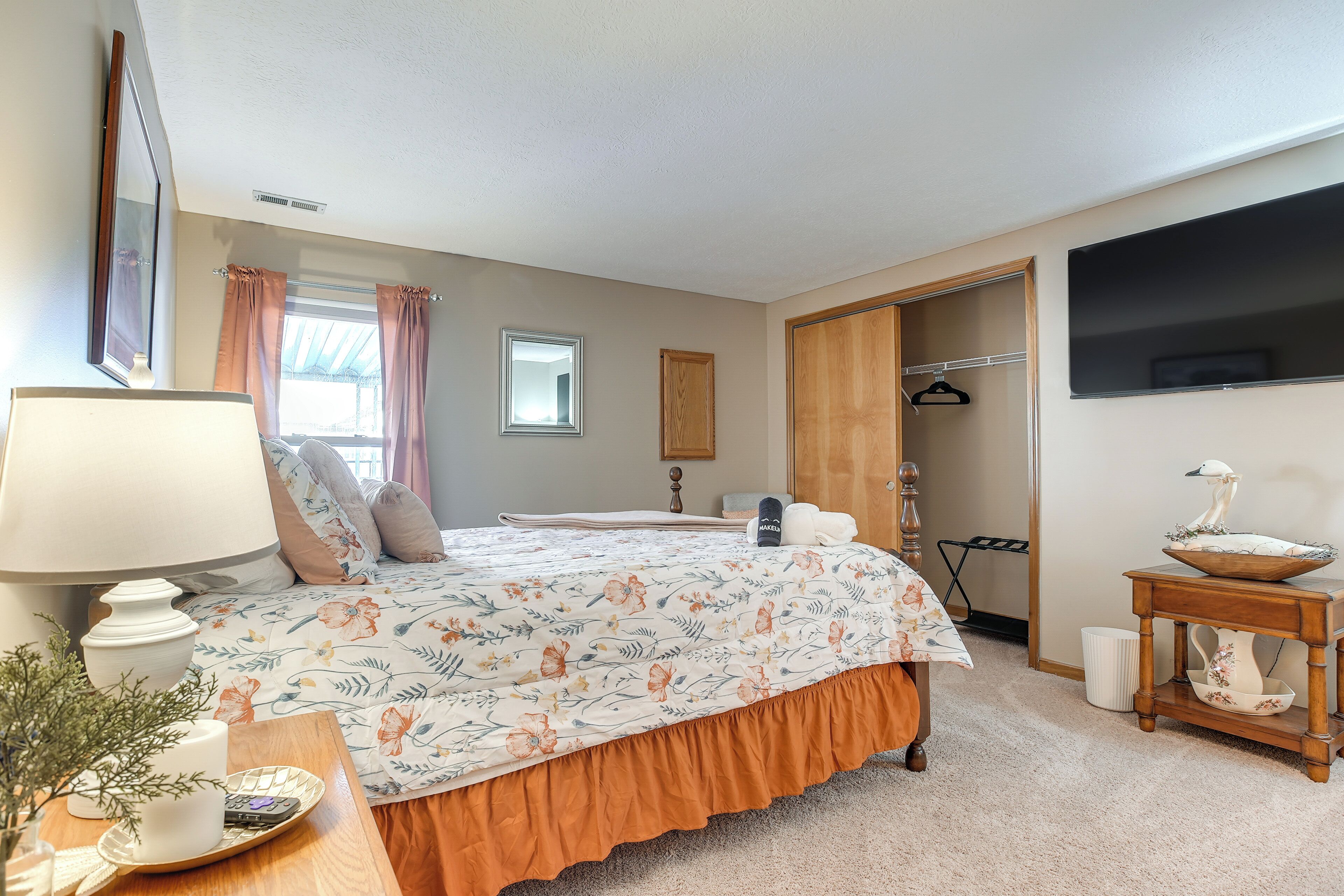 A bedroom with a bed, a bedside table with a lamp, a dresser, a mirror, and a window with curtains.