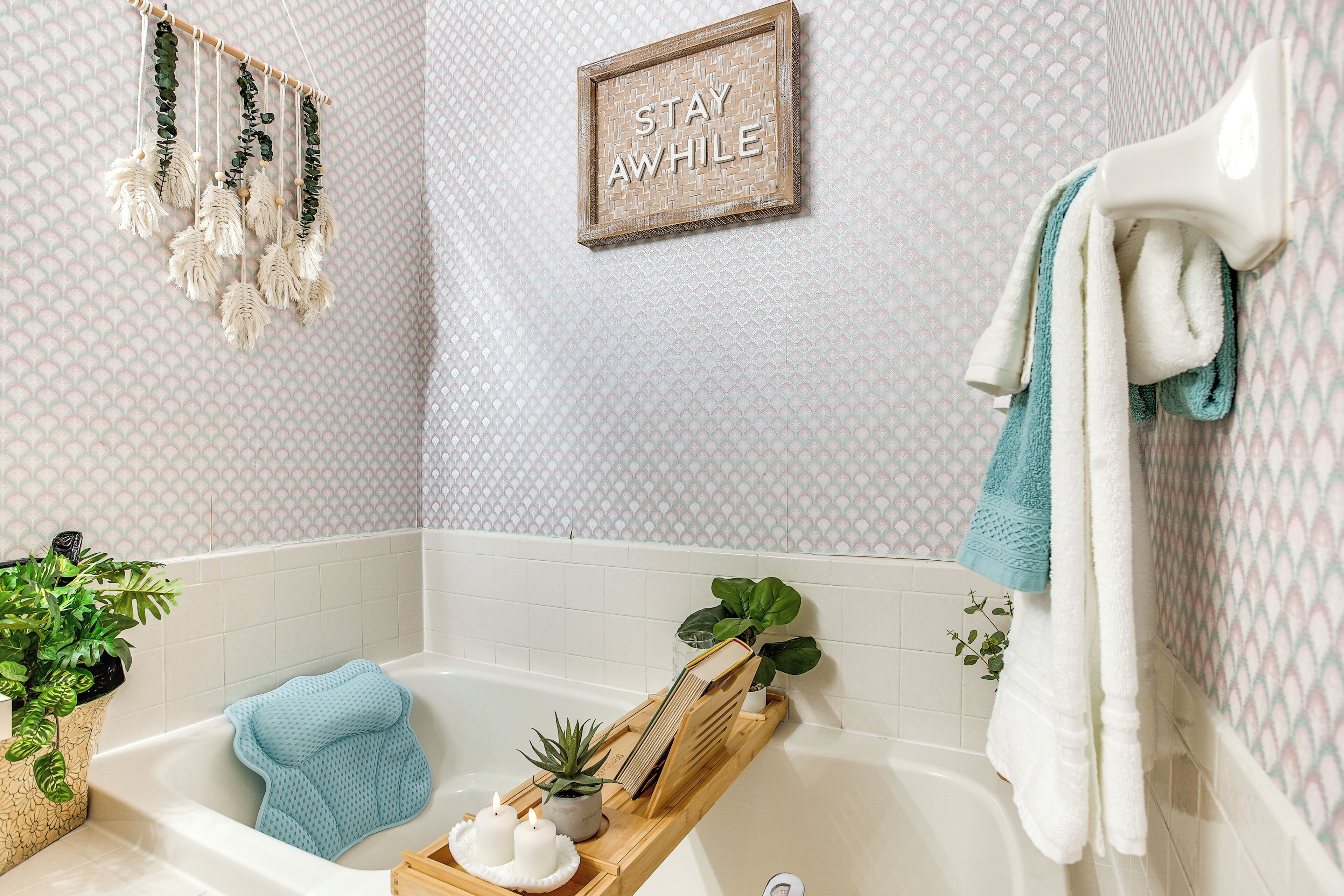 A bathroom with a bathtub, a towel rack, a framed sign, and a decorative wall hanging.
