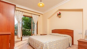 A bedroom with a bed, wooden nightstands, a dresser, a window with curtains, and a small wall decoration. - Kalkan Center 2+1 Villa in Nature - Variola (Antalya)