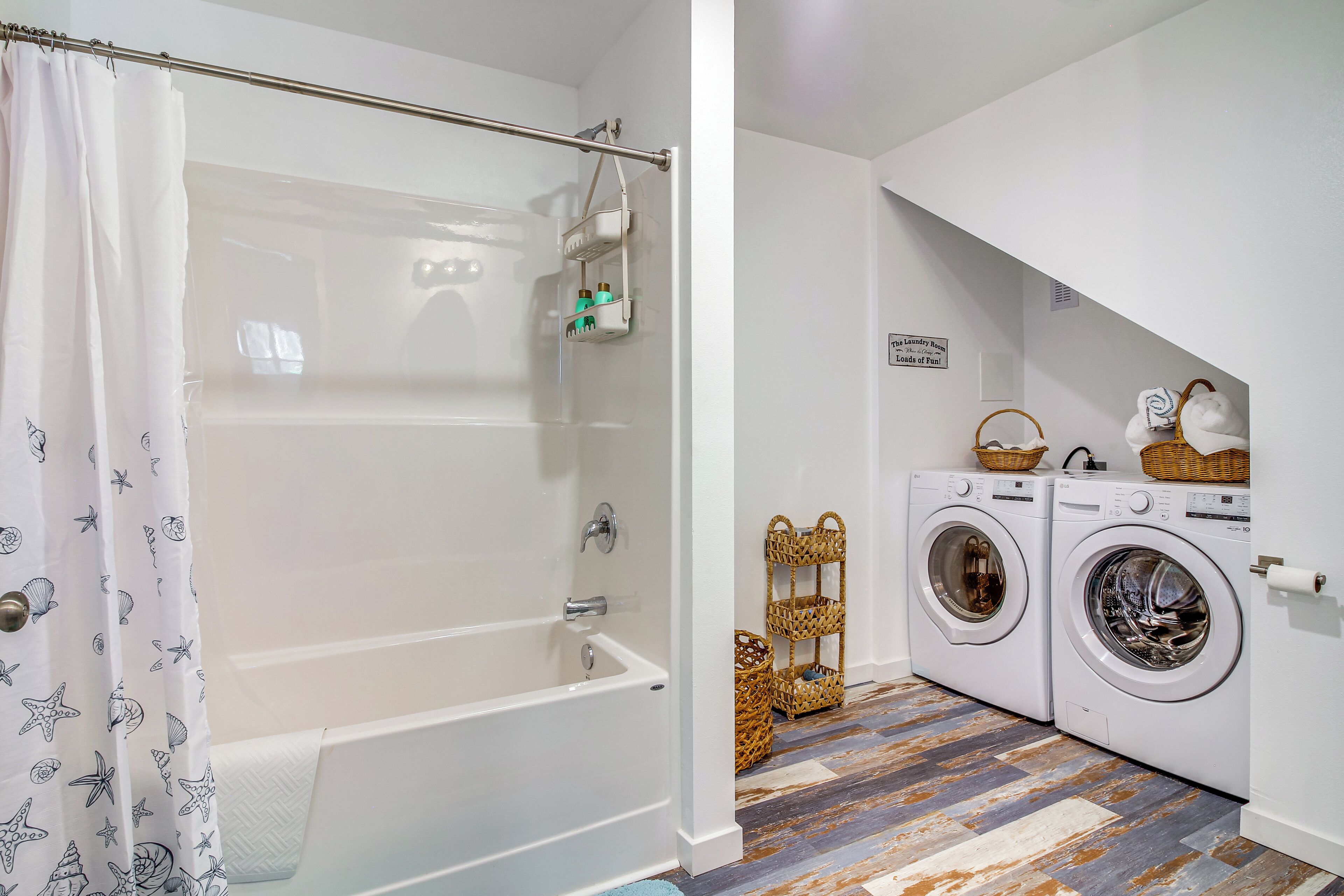 A bathroom with a bathtub, a shower curtain, a towel rack, a washing machine, and a laundry basket.