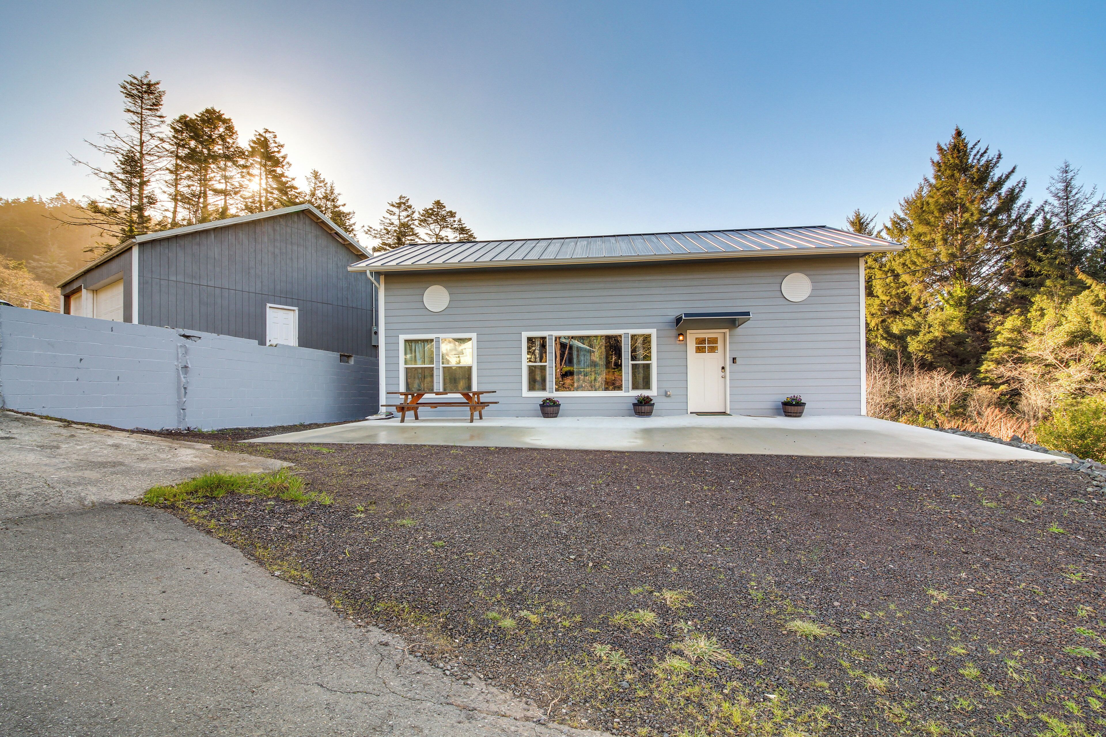 A modern single-story house with a grey exterior, a front porch with a bench, and a small garden area.