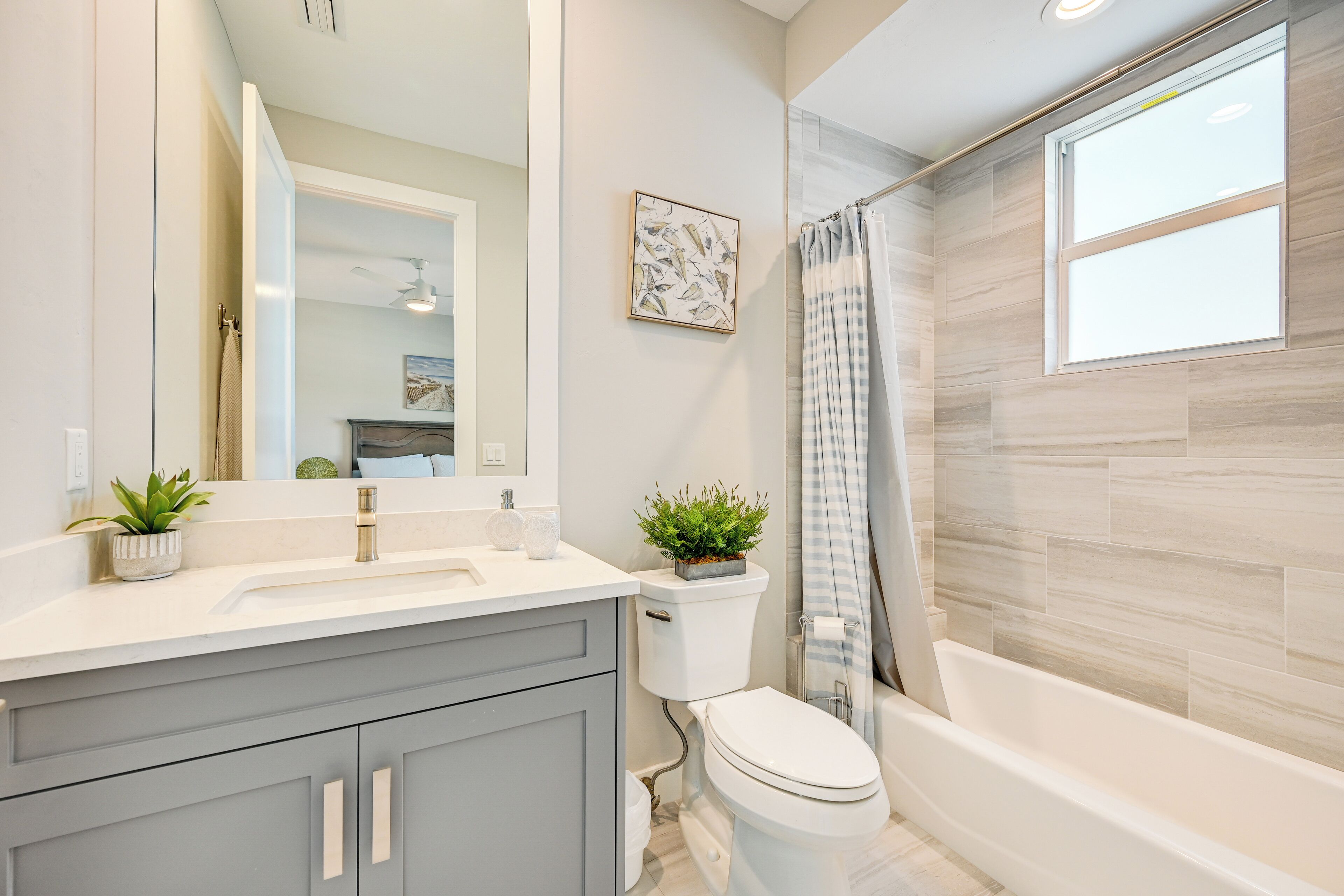 A modern bathroom with a white sink, grey cabinets, a toilet, and a bathtub.