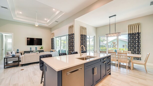 A modern kitchen with a central island, a dining area with wooden chairs, and a large window with patterned curtains. - Luxury Marco Island Escape W/pool & Spa Retreat (Marco Island)