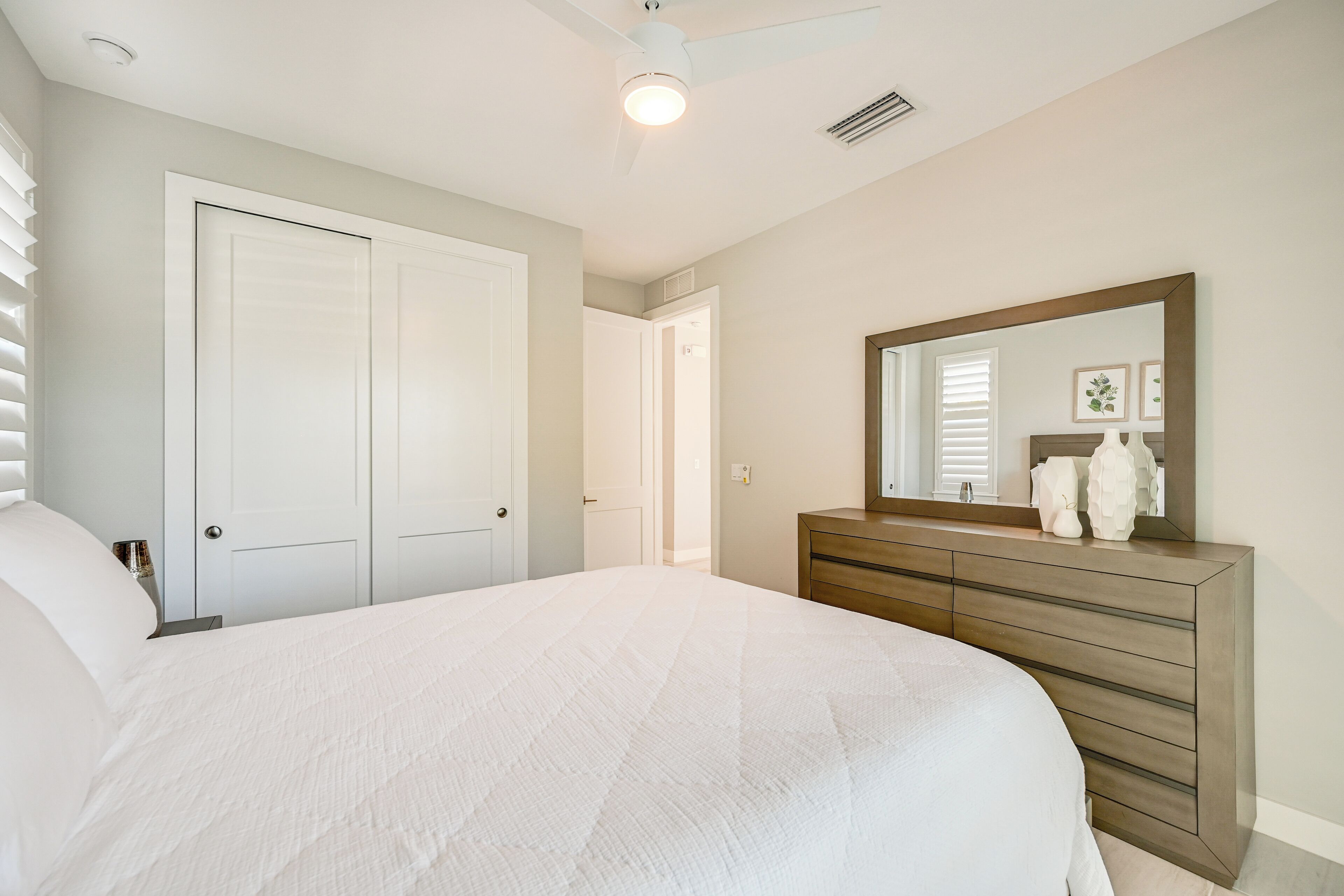 A bedroom with a large bed, a dresser, a mirror, and a door leading to another room.