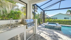 A kitchen with a built-in grill, a sink, and a view of a pool and greenery outside. - Luxury Marco Island Escape W/pool & Spa Retreat (Marco Island)