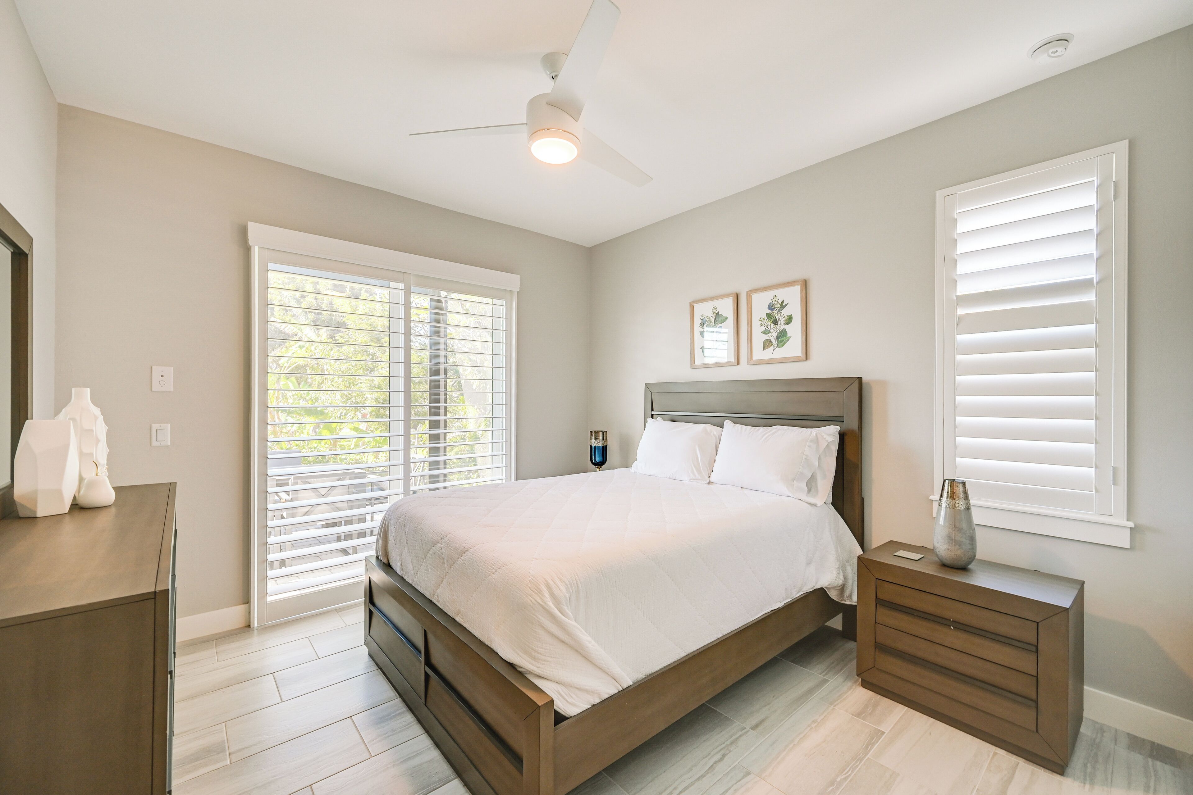 A bedroom with a bed, nightstands, a dresser, and a ceiling fan.