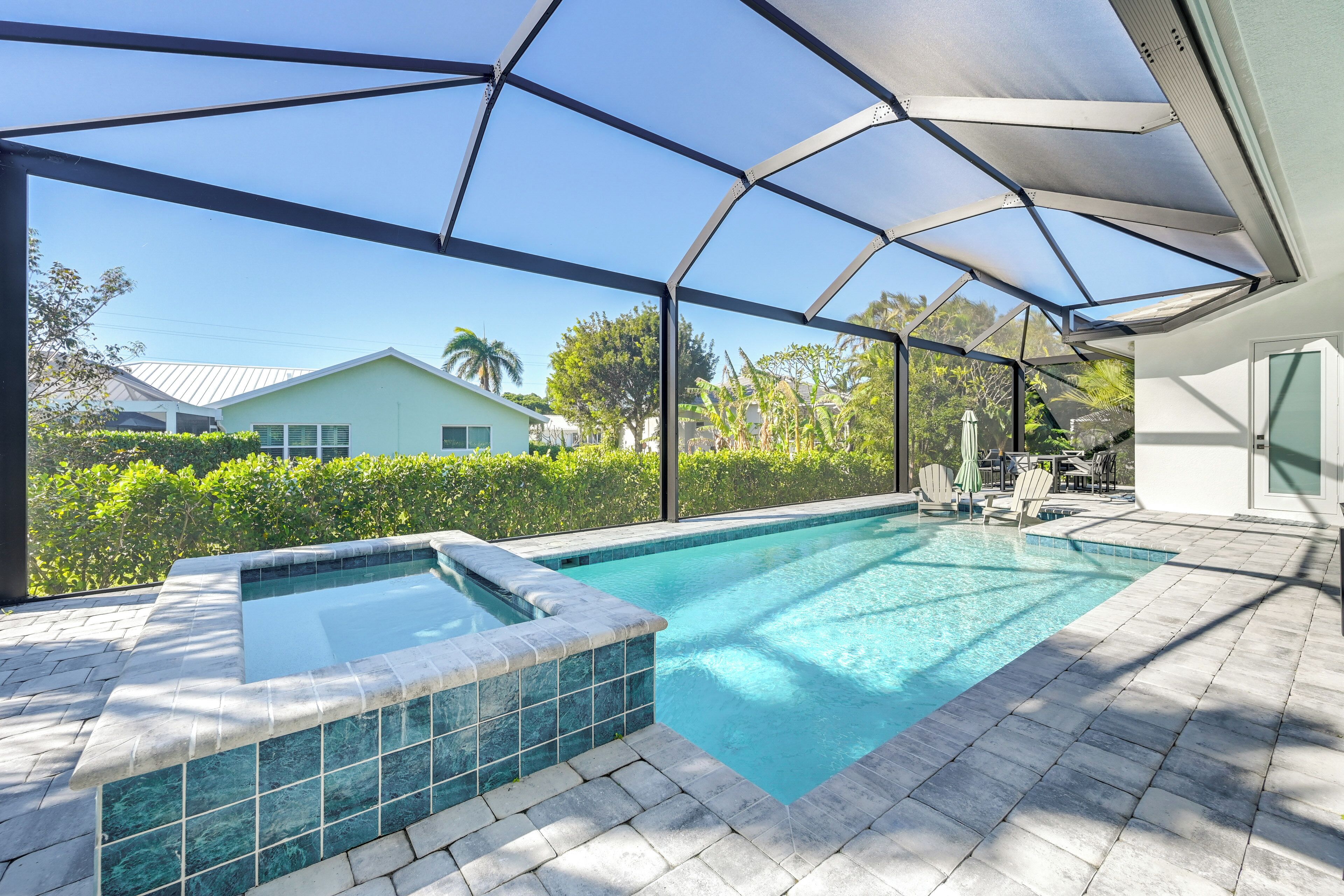 A covered outdoor swimming pool with a hot tub, surrounded by a patio area with chairs and a table.