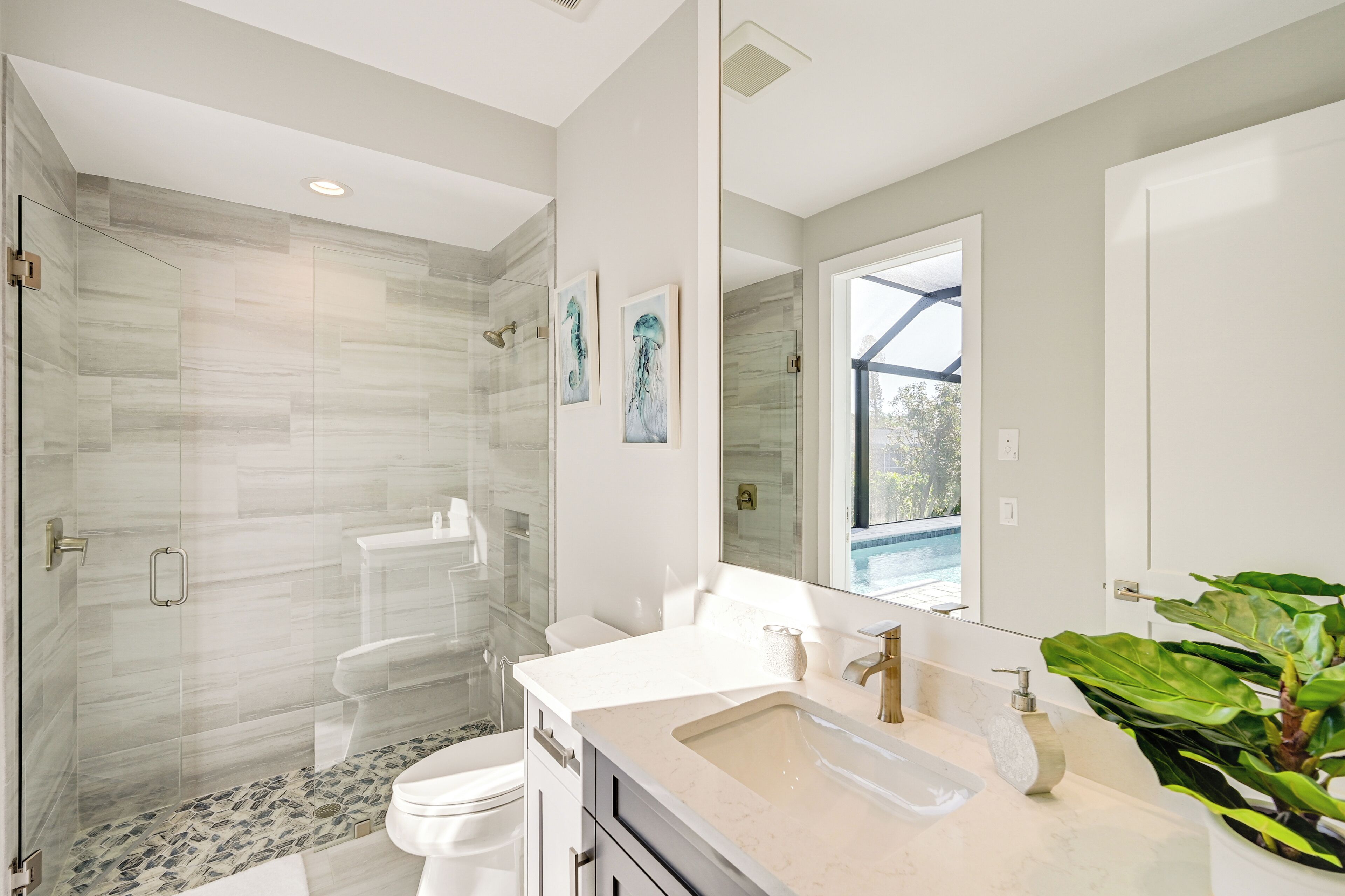 A modern bathroom with a glass-enclosed shower, a large mirror, and a sink with a marble countertop.