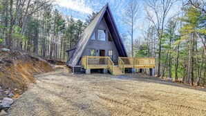 A triangular cabin with a wooden deck and stairs, surrounded by a forest.