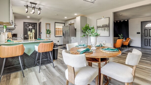 A modern kitchen with a dining area, featuring a wooden dining table, white upholstered chairs, and a central island with bar stools.