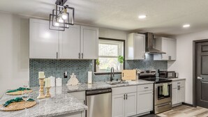 A modern kitchen with white cabinets, a granite countertop, stainless steel appliances, and a window with a view of trees.