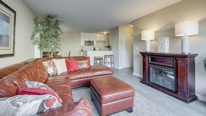 A living room with a brown leather sectional sofa, a fireplace, and a kitchen in the background.