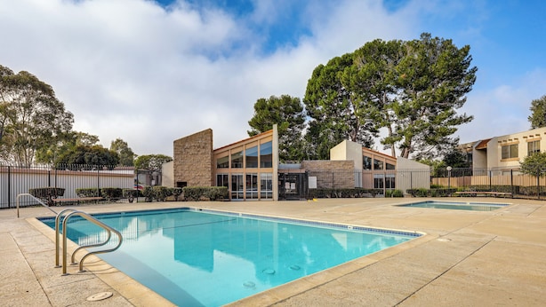A swimming pool with a clear blue water surface, surrounded by a paved area and a fence.