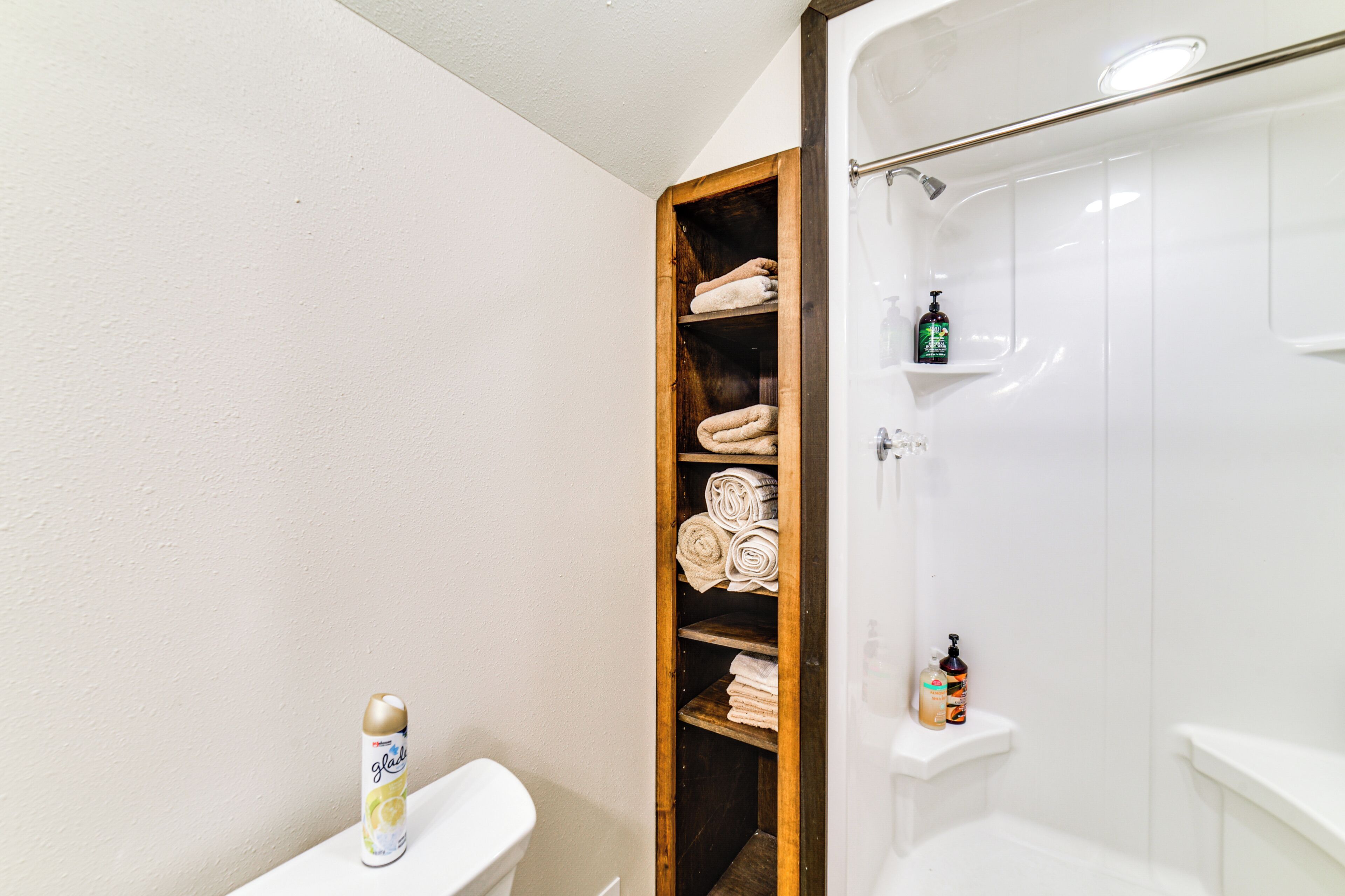 Un baño con un estante de madera que contiene toallas, un inodoro y una zona de ducha.