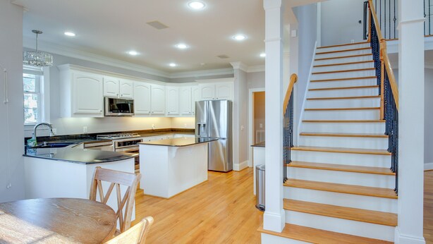 A modern kitchen with white cabinets, stainless steel appliances, and a wooden dining table. - Executive Wfh-friendly Haven in Blythewood! (Blythewood)