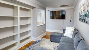 A modern living room with built-in shelving, a grey sofa, a patterned rug, and a mounted TV. - Executive Wfh-friendly Haven in Blythewood! (Blythewood)