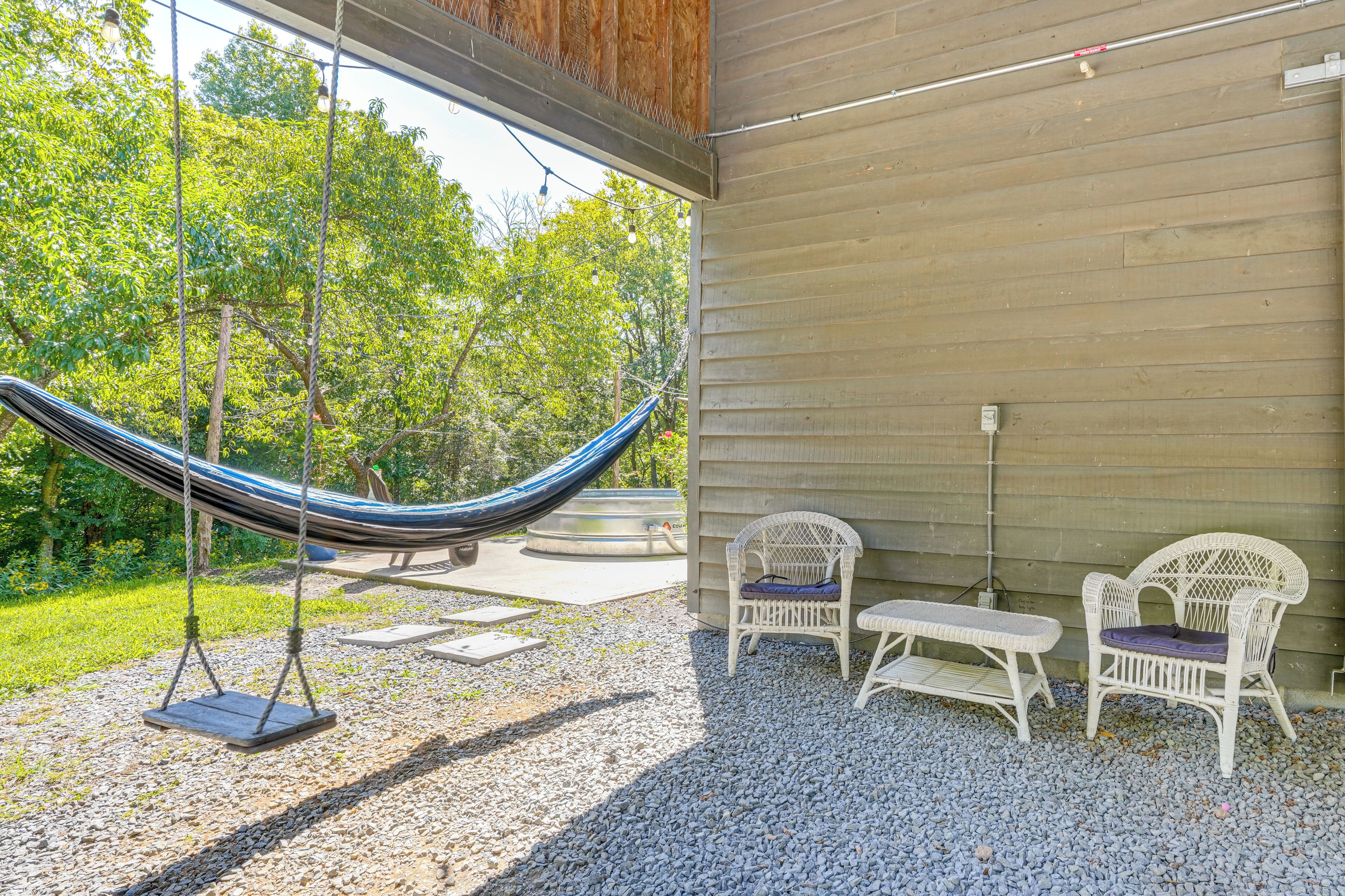 Una hamaca, dos sillones de mimbre y un patio con suelo de grava y pared de madera.