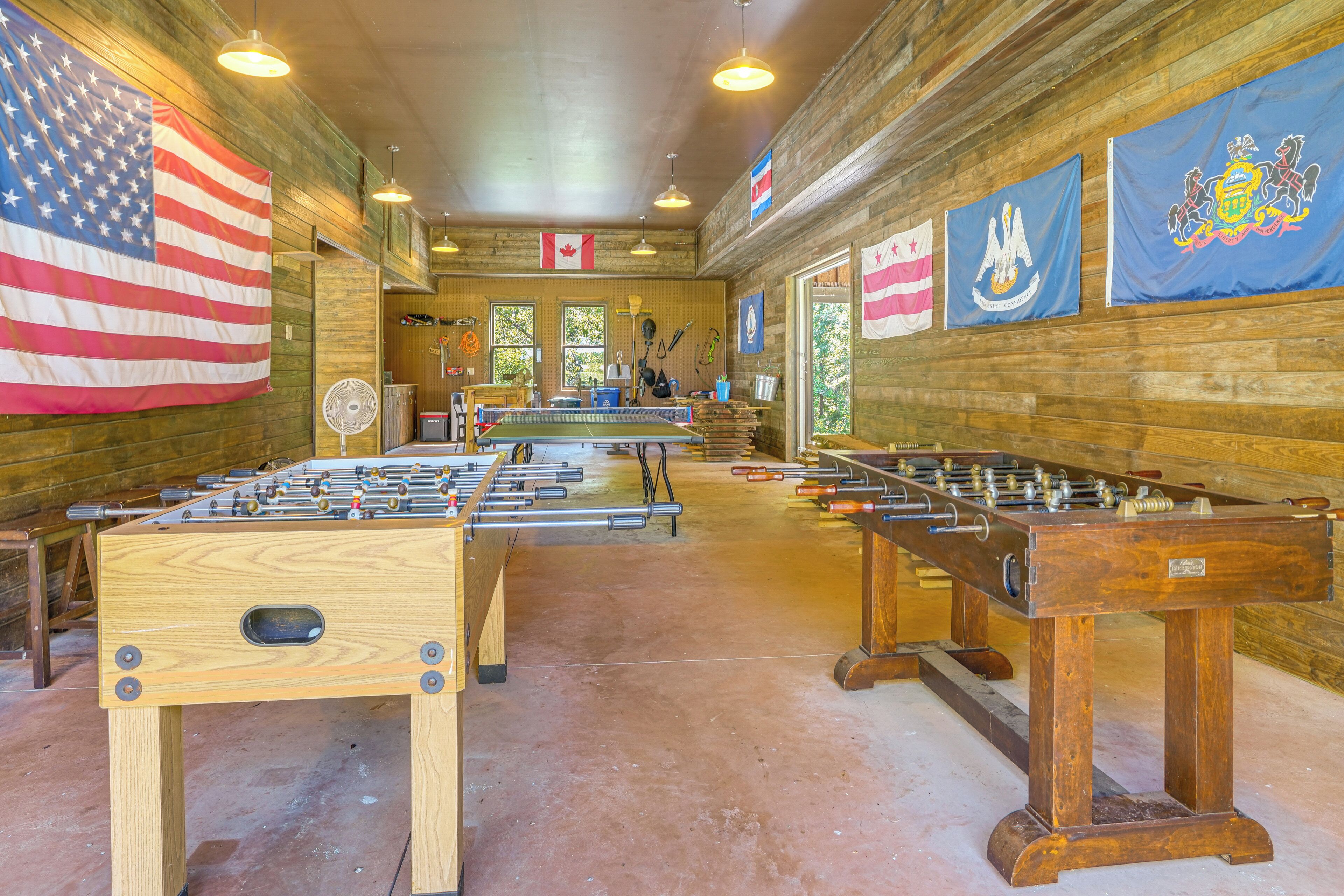 A room with wooden walls, multiple foosball tables, and various flags including the American flag and others.