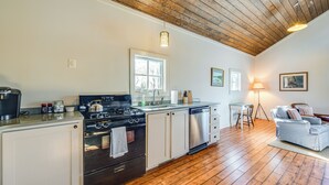 A kitchen with a wooden ceiling, white cabinets, a stove, and a dishwasher. There is a dining area with a table and chairs, and a sofa. - Countryside Barndominium in Virginia w/ Patio (Louisa)