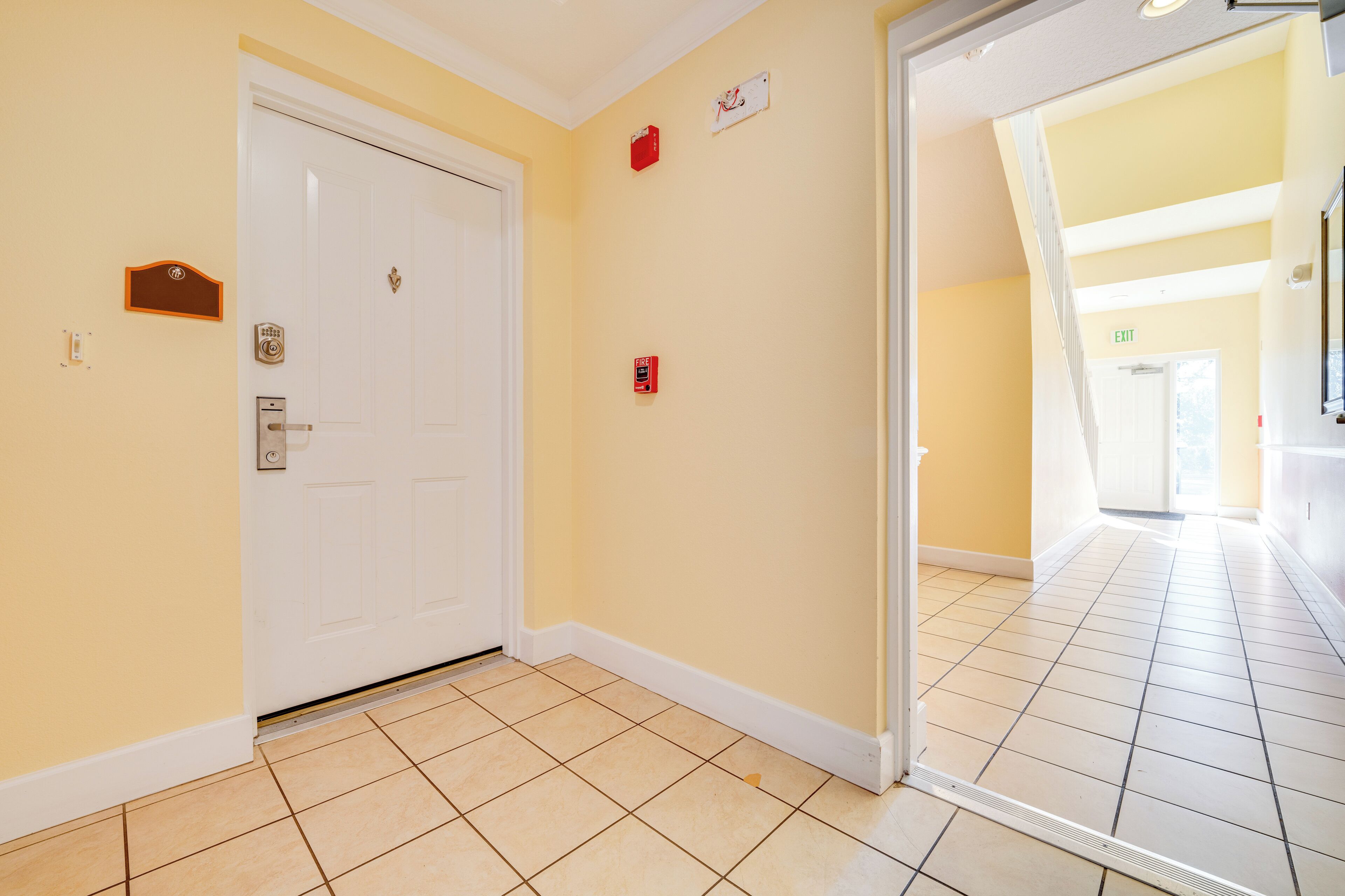 A hallway with a white door, a fire alarm, and an exit sign.