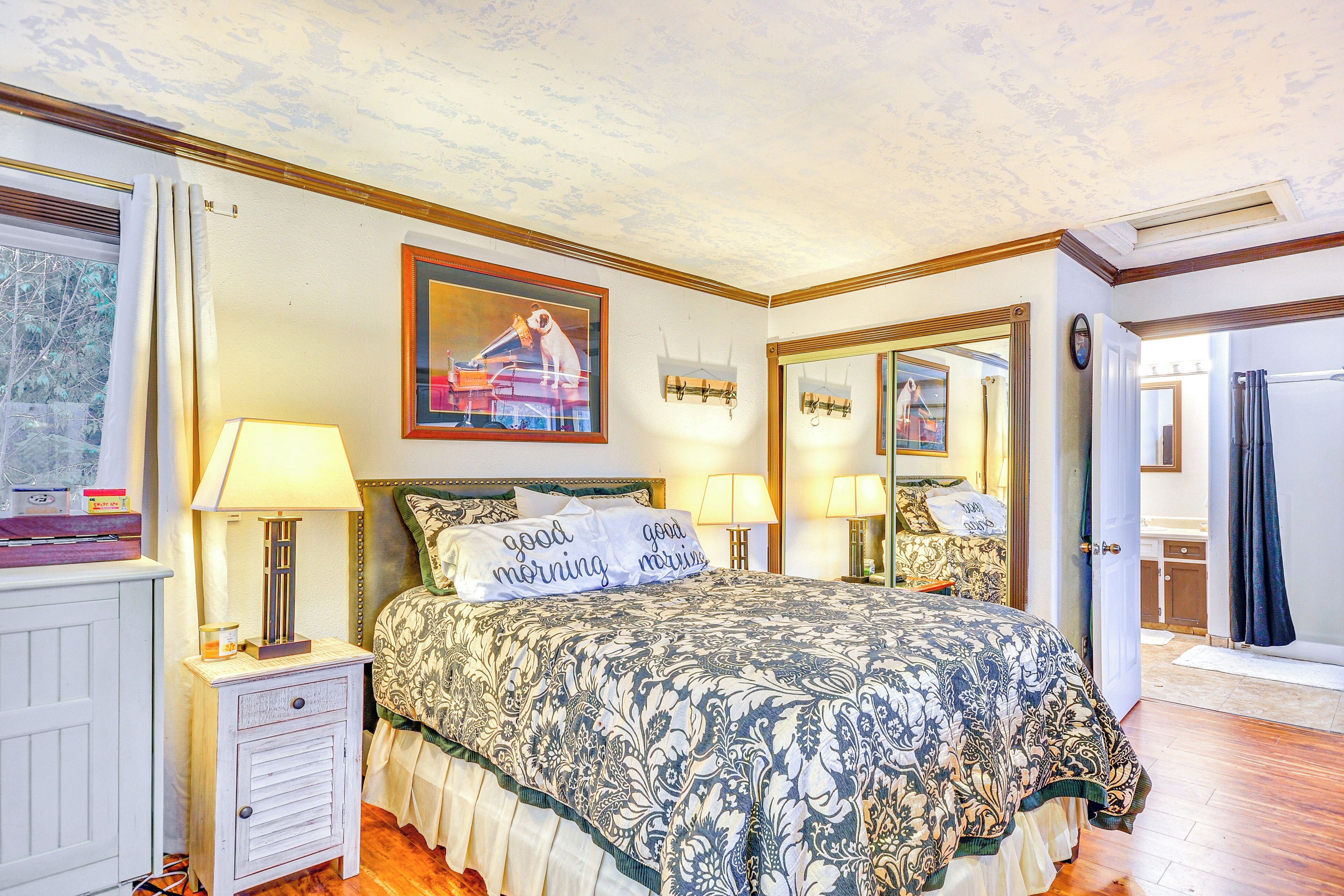 A bedroom with a bed, two bedside lamps, a nightstand, a mirror, and a window with curtains.