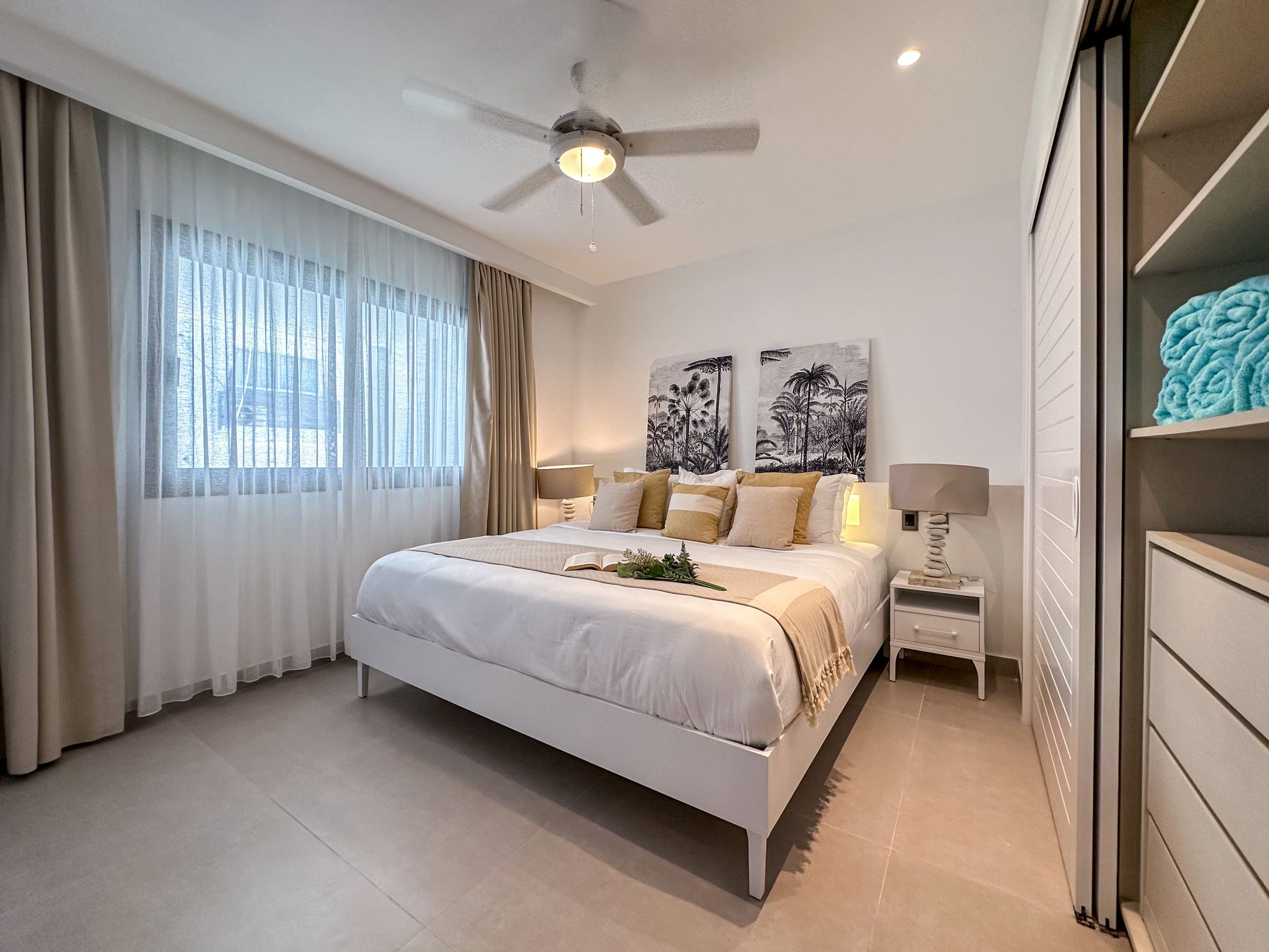 A modern bedroom with a large bed, a ceiling fan, and artwork on the wall.