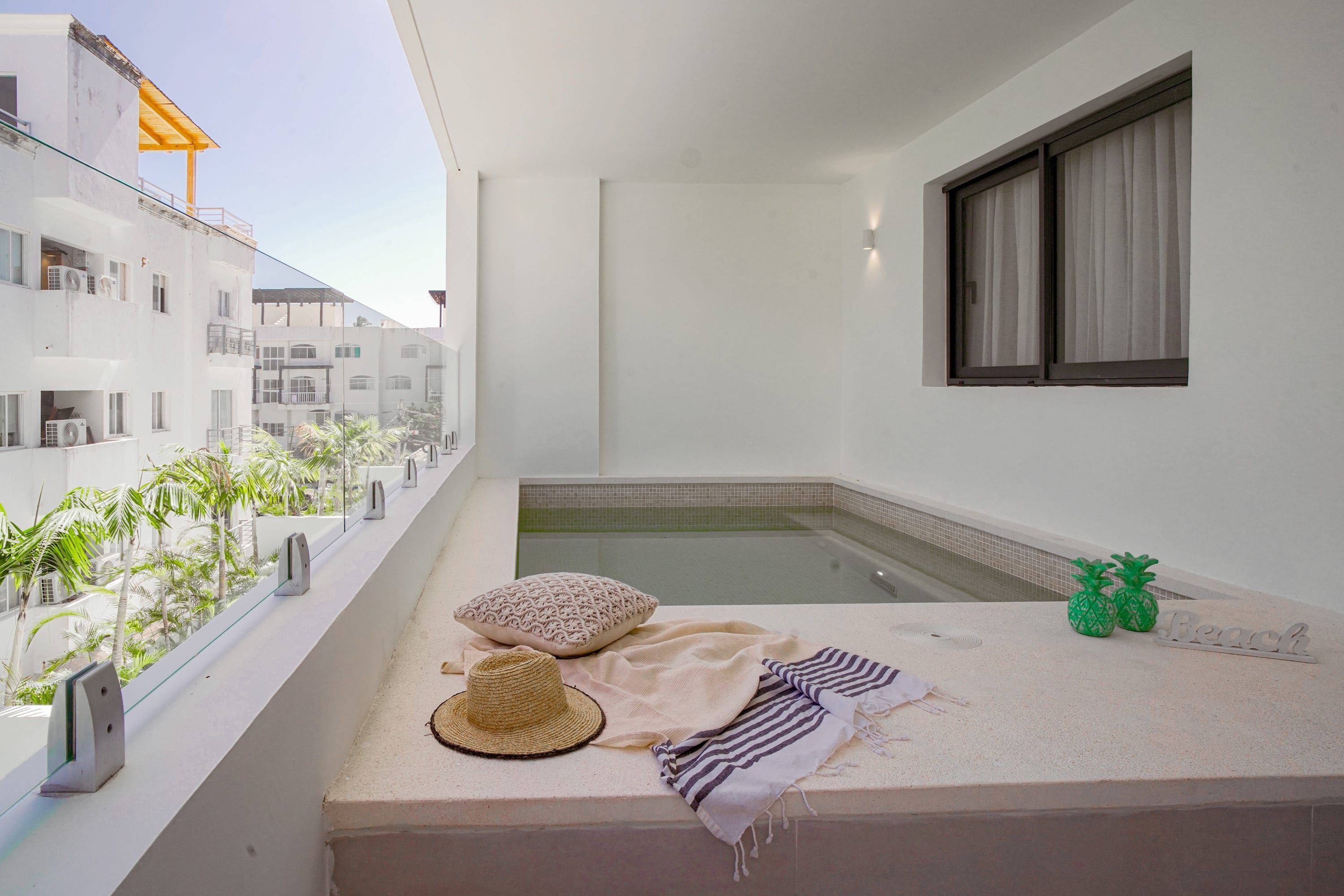Un balcón con una piscina pequeña, una toalla, un sombrero y cojines decorativos.