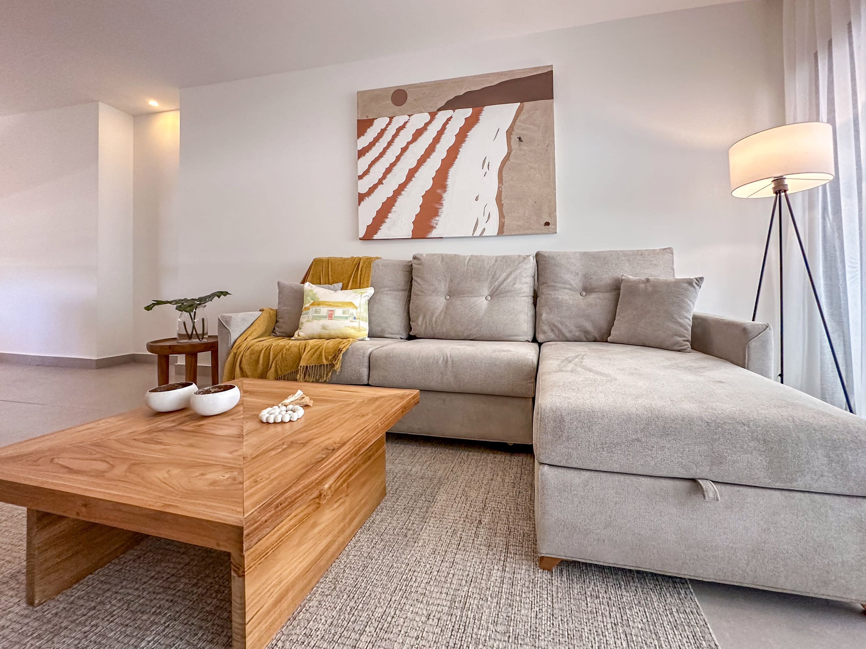 Una sala de estar moderna con un sofá seccional gris, una mesa de centro de madera, una planta pequeña y una lámpara de pie.