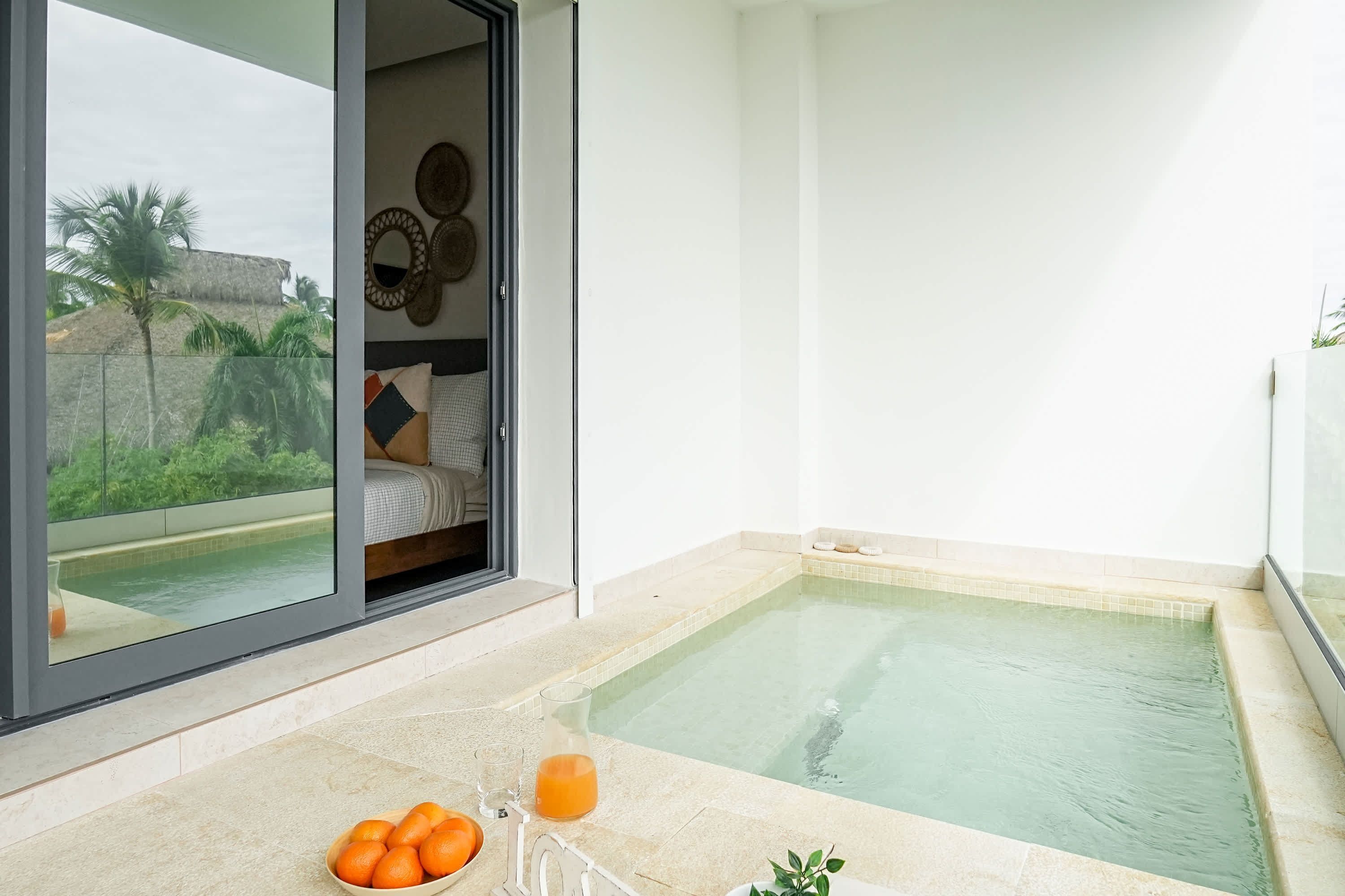 Un baño moderno con bañera, cabina de ducha de vidrio y vistas a una piscina y palmeras.