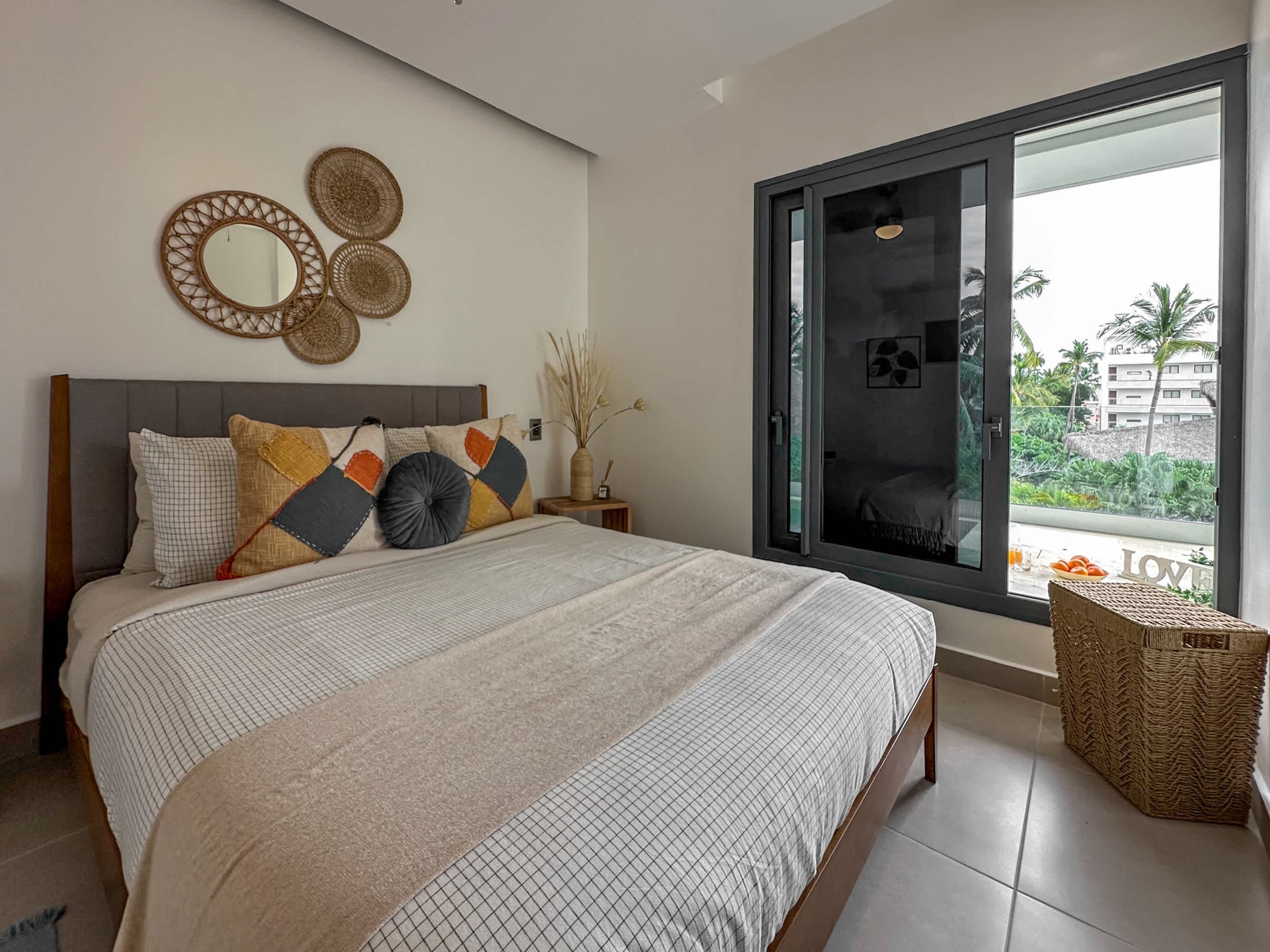 Een moderne slaapkamer met een groot bed, uitzicht op de natuur via een schuifdeur en decoratieve wandkunst.
