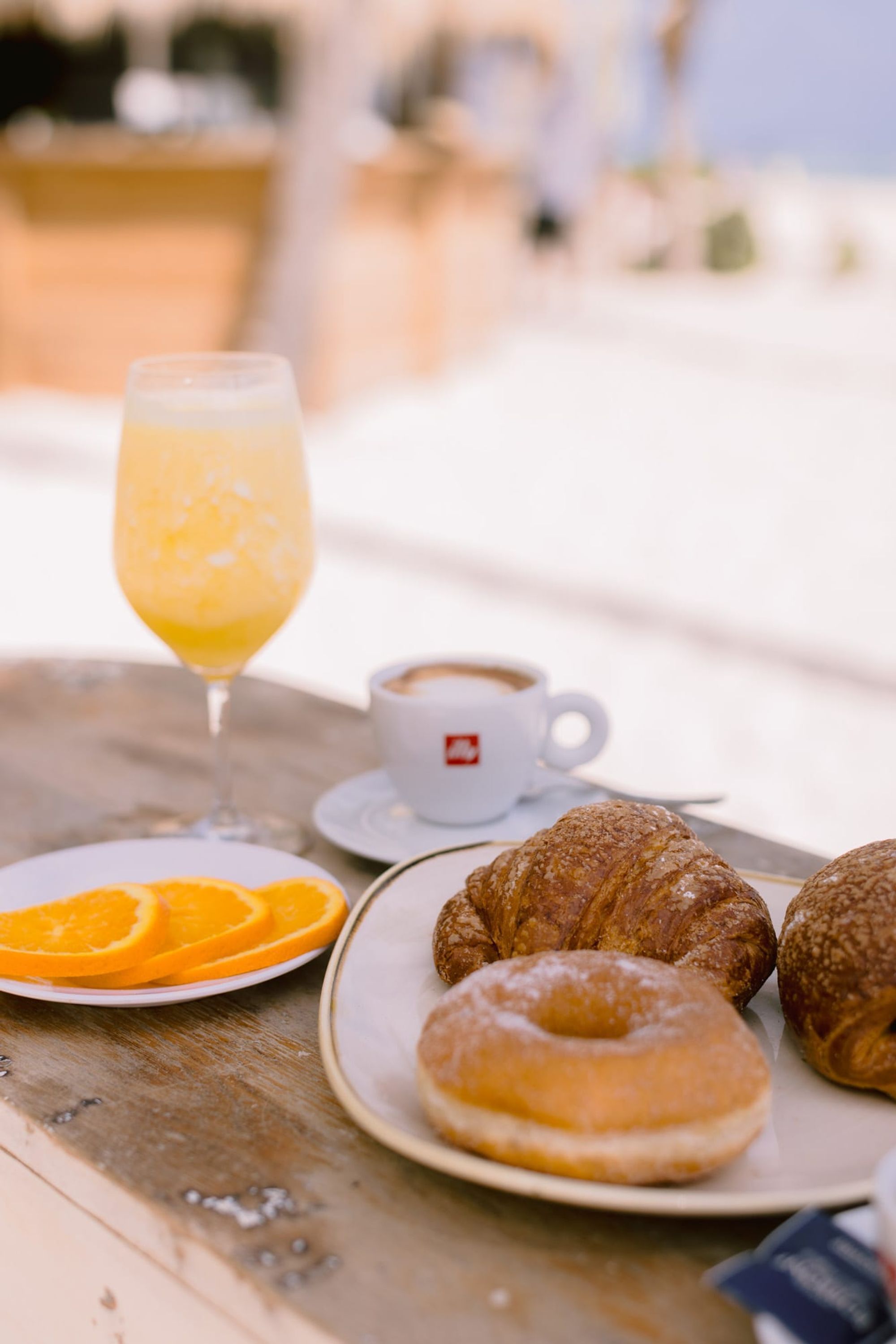 A breakfast table with croissants, orange slices, a glass of orange juice, and a cup of coffee.