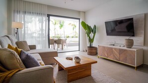 A modern living room with a sofa, coffee table, TV, and a large window with a view of palm trees. - Luxury 3 Bedroom Apartment at the Beach (Punta Cana)