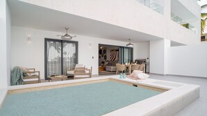 A modern indoor swimming pool with a tiled floor, surrounded by seating areas and a view of the interior space. - Luxury 3 Bedroom Apartment at the Beach (Punta Cana)