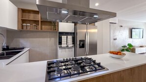 A modern kitchen with a stainless steel range hood, a built-in oven, a refrigerator, and a gas stove. - Spectacular Brand new Beach Condo (Punta Cana)