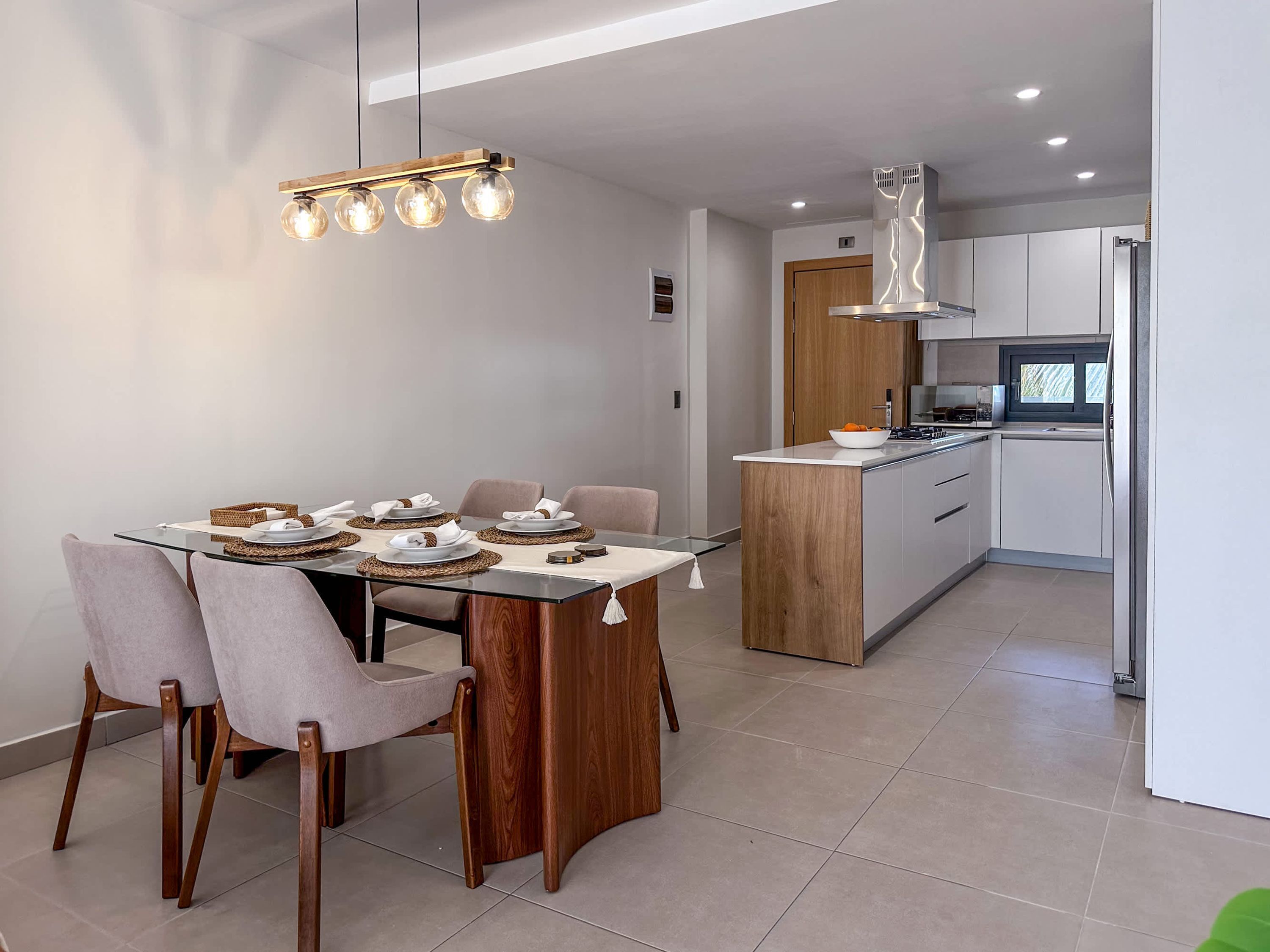 A modern kitchen with white cabinets, a wooden island, and a dining area with a glass table and cushioned chairs.