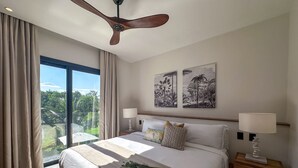 A bedroom with a large bed, two bedside tables with lamps, a ceiling fan, and artwork on the wall. - Spectacular Golf Front 3BR Apartment! (Punta Cana)