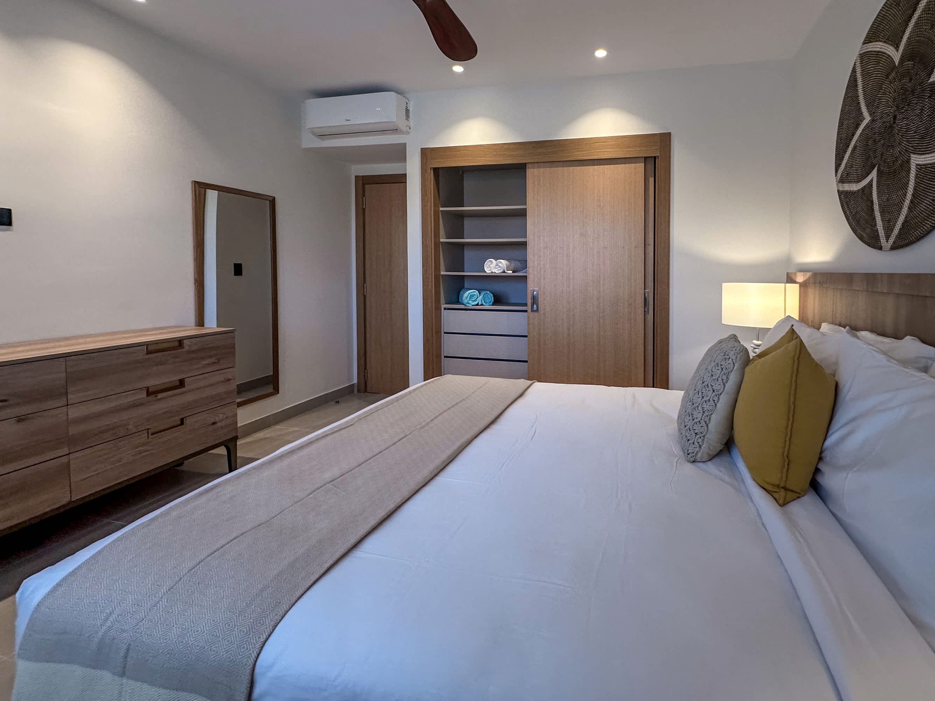 Une chambre à coucher comprenant un lit, une commode en bois, une armoire et un ventilateur de plafond.