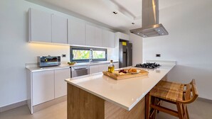 Une cuisine moderne avec des meubles blancs, un îlot central et une hotte de cuisine en acier inoxydable.