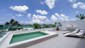 Une piscine sur le toit offrant une vue sur l’océan, des chaises longues et des plantes en pot.