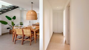 Un espace repas moderne avec une table et des chaises en bois, un luminaire suspendu en osier et une plante en pot.